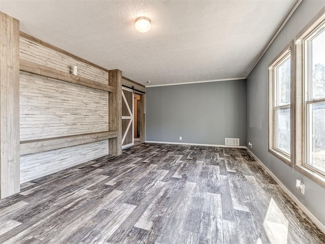 unfurnished living room featuring a barn door, a wealth of natural light, crown molding, and dark hardwood / wood-style floors