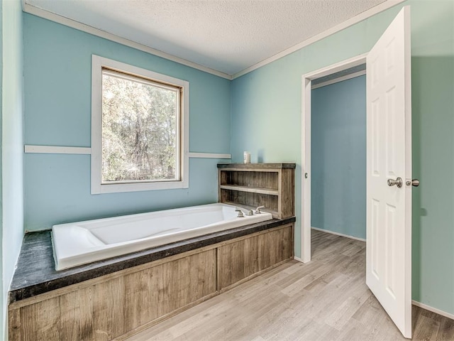 bathroom featuring a bathing tub, wood-type flooring, a textured ceiling, and ornamental molding