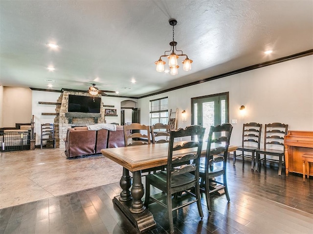 dining space with a fireplace, hardwood / wood-style floors, ceiling fan with notable chandelier, and crown molding