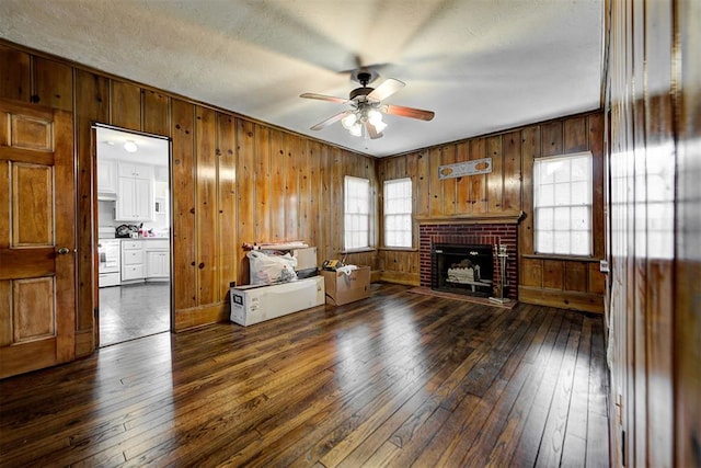 living room with dark hardwood / wood-style flooring, a brick fireplace, ceiling fan, and wooden walls