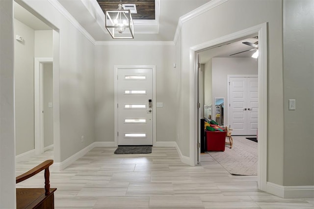 foyer with ceiling fan with notable chandelier, ornamental molding, and a raised ceiling