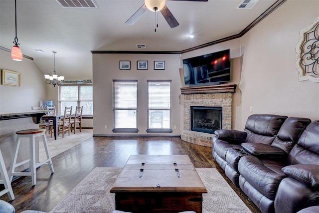 living room featuring hardwood / wood-style floors, vaulted ceiling, a fireplace, ceiling fan with notable chandelier, and ornamental molding