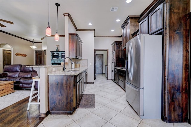 kitchen with light stone countertops, sink, hanging light fixtures, stainless steel fridge, and light tile patterned floors