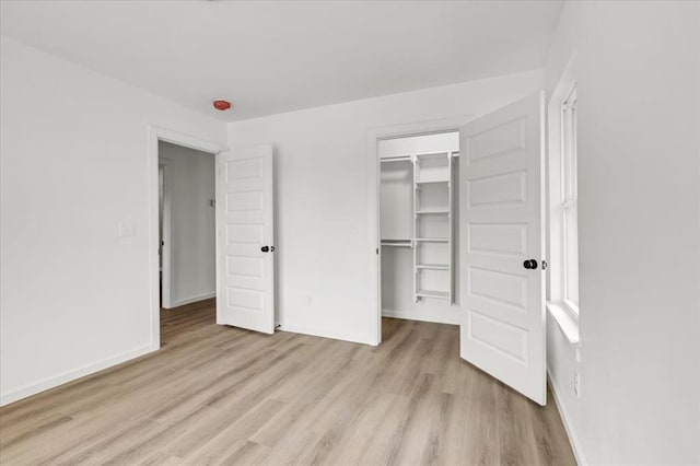 unfurnished bedroom with a walk in closet, a closet, and light wood-type flooring