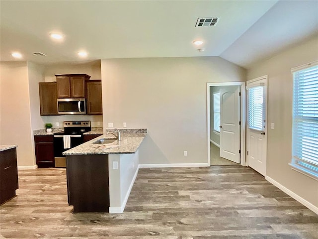 kitchen featuring lofted ceiling, sink, light stone countertops, light wood-type flooring, and stainless steel appliances