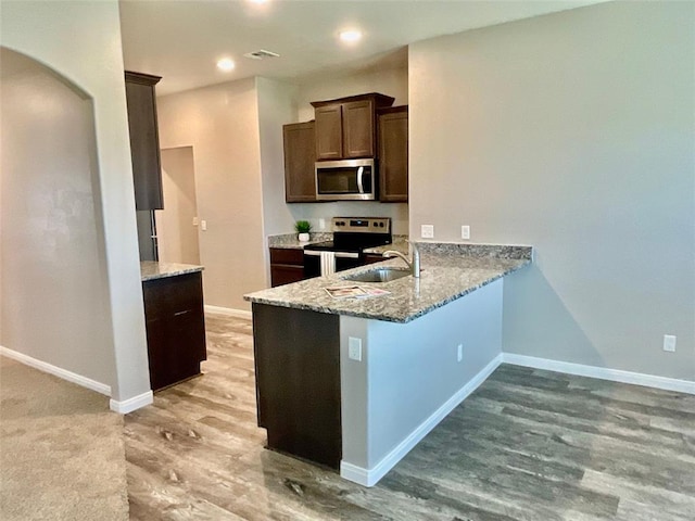 kitchen with dark brown cabinetry, sink, stainless steel appliances, light stone counters, and light wood-type flooring