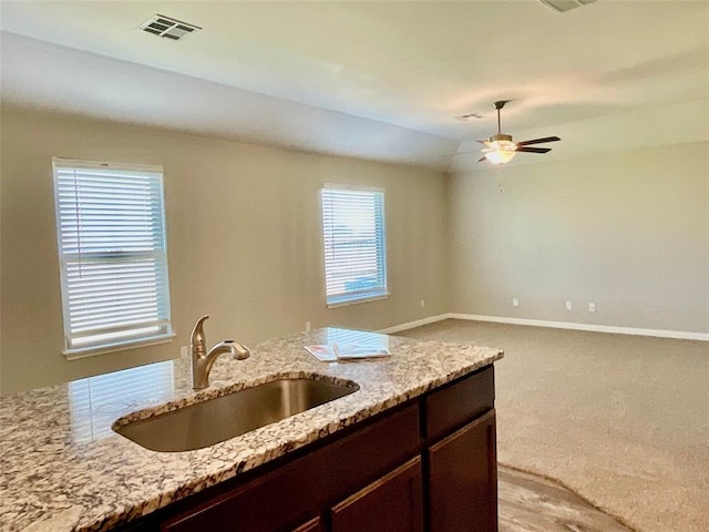 kitchen with sink, ceiling fan, light stone countertops, light colored carpet, and dark brown cabinetry