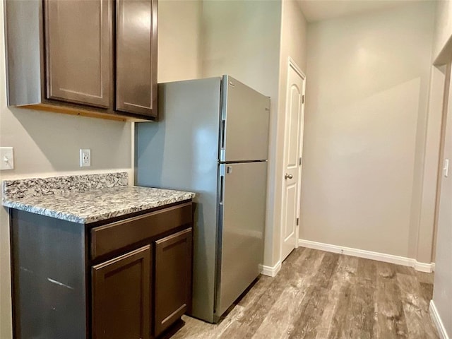 kitchen featuring dark brown cabinetry, stainless steel fridge, light hardwood / wood-style floors, and light stone counters