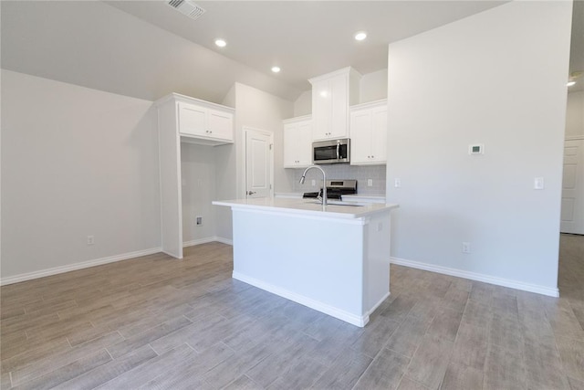 kitchen featuring light countertops, stainless steel microwave, visible vents, white cabinets, and an island with sink