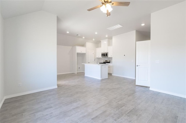 unfurnished living room with baseboards, vaulted ceiling, light wood finished floors, and ceiling fan