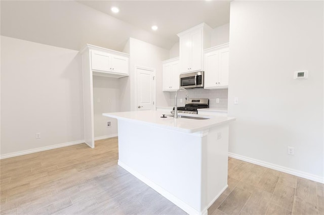 kitchen with white cabinets, a sink, light countertops, appliances with stainless steel finishes, and a kitchen island with sink