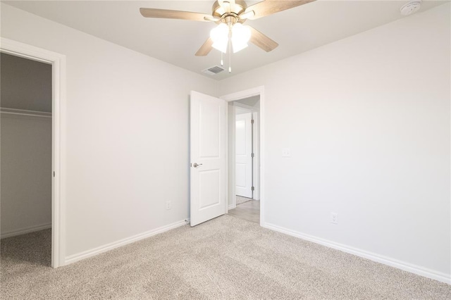 unfurnished bedroom featuring a closet, baseboards, a walk in closet, and light carpet