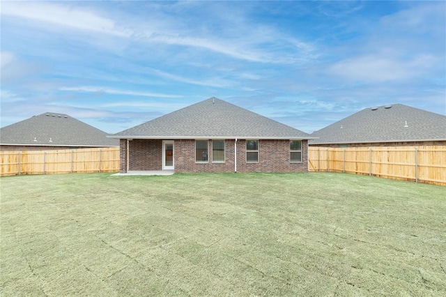 rear view of property with a lawn, a fenced backyard, a patio, brick siding, and roof with shingles