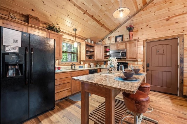 kitchen with pendant lighting, wood walls, black fridge, sink, and light stone countertops