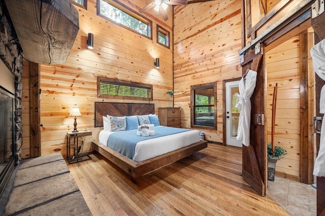 bedroom with a towering ceiling, light hardwood / wood-style flooring, ceiling fan, and wooden walls