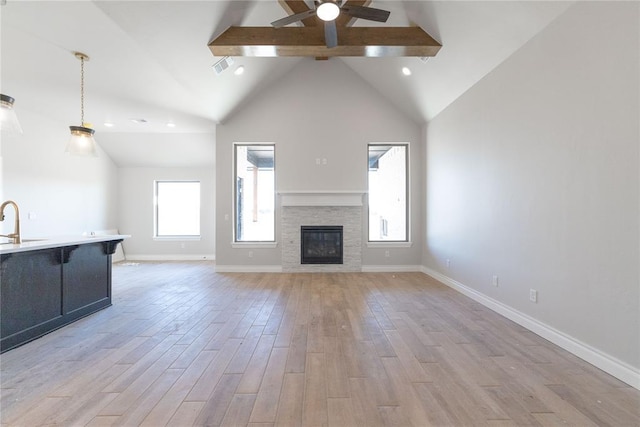 unfurnished living room with high vaulted ceiling, a stone fireplace, a sink, baseboards, and light wood finished floors