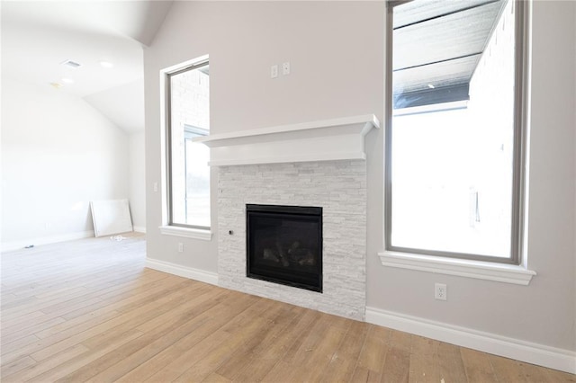 unfurnished living room featuring lofted ceiling, a stone fireplace, baseboards, and wood finished floors