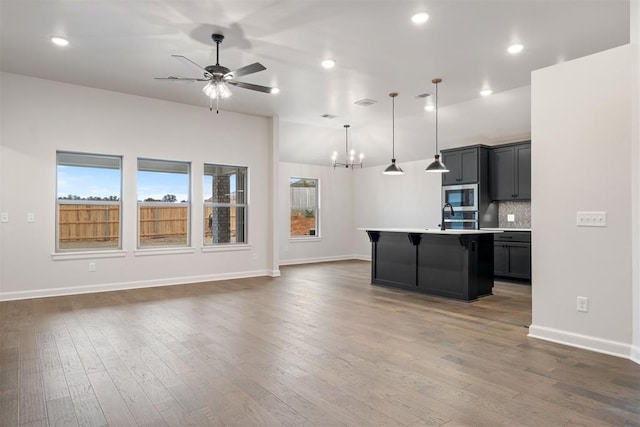 kitchen with hanging light fixtures, appliances with stainless steel finishes, dark hardwood / wood-style floors, and a kitchen island with sink