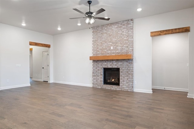 unfurnished living room featuring dark hardwood / wood-style flooring, a brick fireplace, and ceiling fan