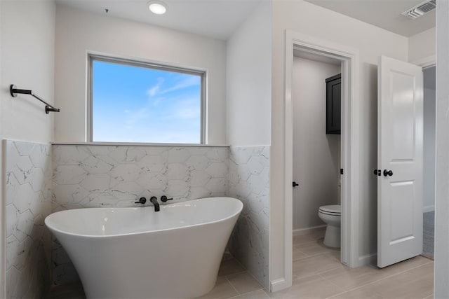 bathroom with a tub to relax in, tile patterned flooring, tile walls, and toilet