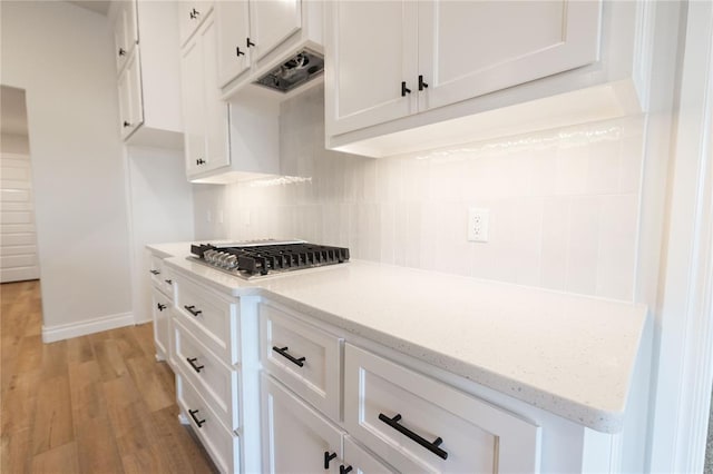 kitchen featuring stainless steel gas cooktop, light wood-type flooring, white cabinetry, and decorative backsplash