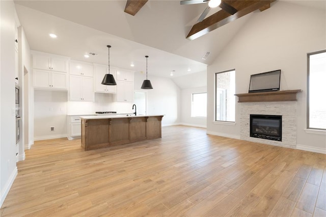 kitchen featuring a sink, white cabinets, open floor plan, light wood-type flooring, and beamed ceiling