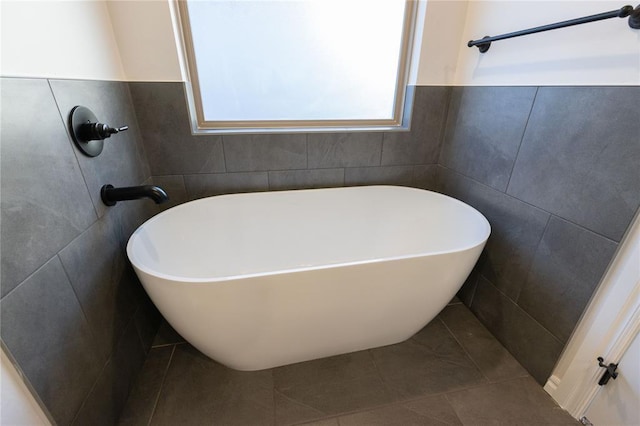 bathroom with tile patterned flooring, a freestanding bath, and tile walls