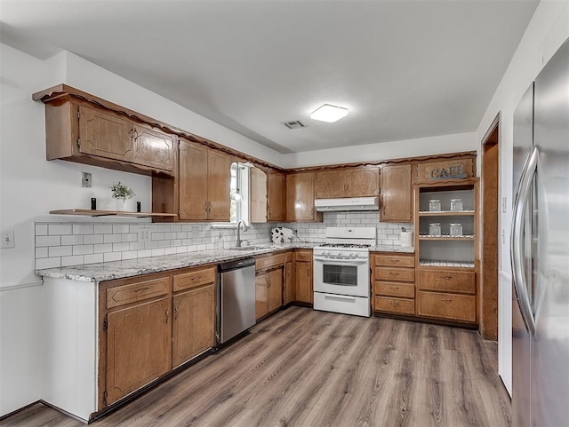 kitchen with backsplash, sink, light stone counters, wood-type flooring, and stainless steel appliances