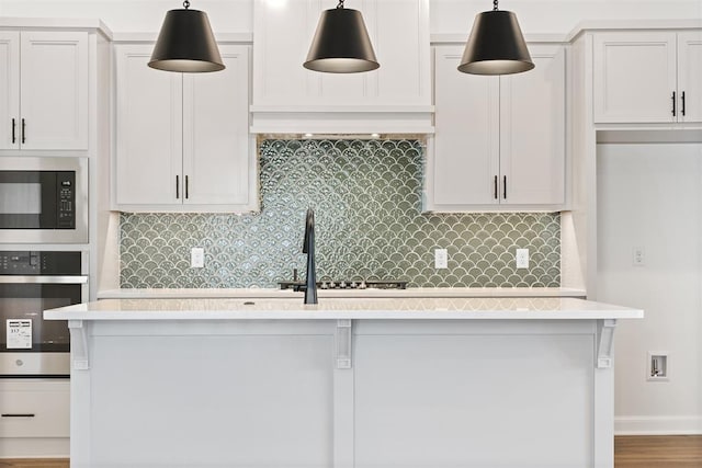 kitchen with pendant lighting, hardwood / wood-style flooring, decorative backsplash, appliances with stainless steel finishes, and white cabinetry