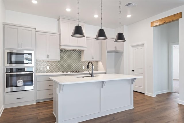 kitchen with sink, dark hardwood / wood-style floors, pendant lighting, a center island with sink, and appliances with stainless steel finishes