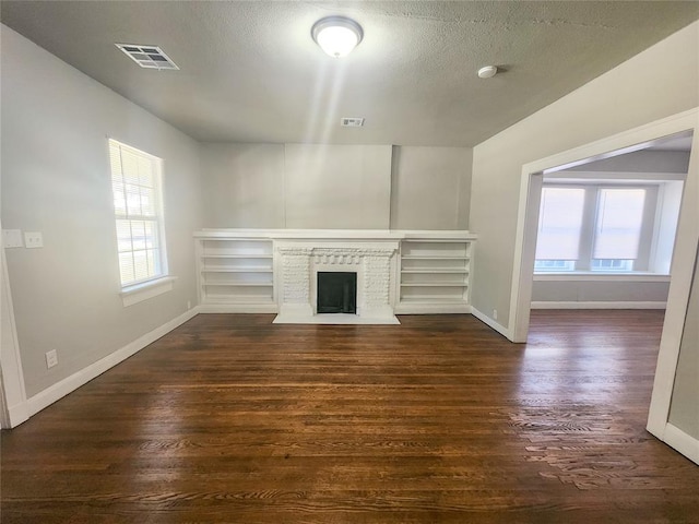 unfurnished living room with a textured ceiling, dark wood-type flooring, and a brick fireplace