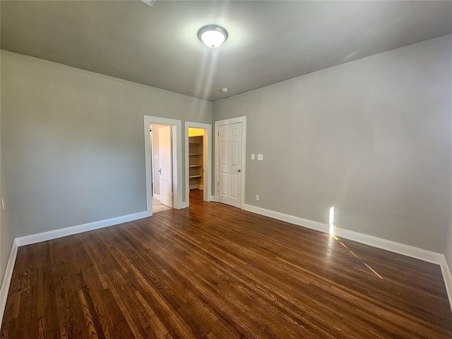 unfurnished bedroom with a spacious closet, a closet, and dark wood-type flooring