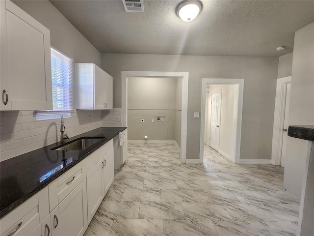 kitchen featuring sink, backsplash, dark stone counters, a textured ceiling, and white cabinets