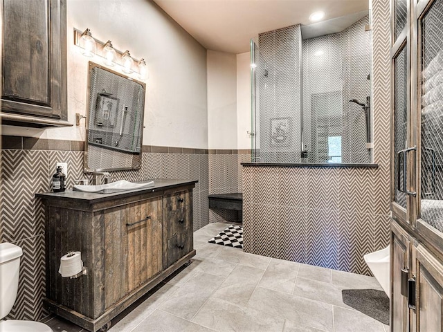 bathroom featuring tile patterned floors, toilet, tiled shower, vanity, and tile walls