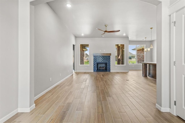 unfurnished living room featuring a tile fireplace, ceiling fan with notable chandelier, and light wood-type flooring
