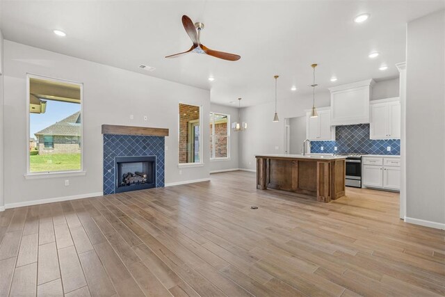 kitchen with white cabinets, a center island with sink, hanging light fixtures, light wood-type flooring, and a fireplace