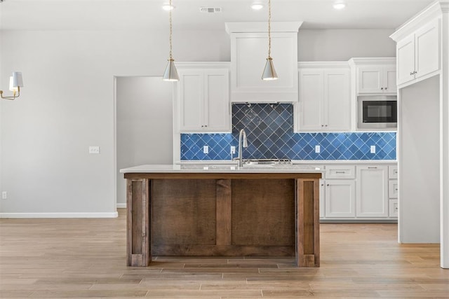 kitchen featuring white cabinetry, stainless steel microwave, hanging light fixtures, and light hardwood / wood-style flooring