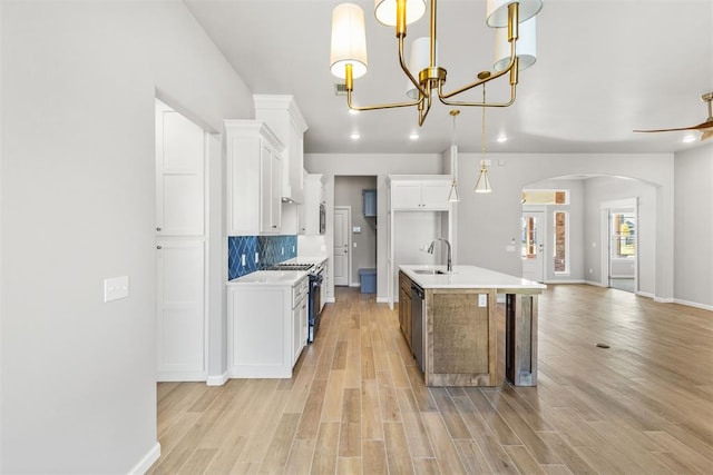 kitchen with a kitchen island with sink, white cabinets, hanging light fixtures, light hardwood / wood-style flooring, and stainless steel appliances