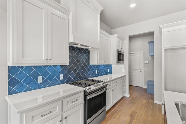kitchen featuring white cabinetry, stainless steel appliances, tasteful backsplash, light stone counters, and light hardwood / wood-style floors