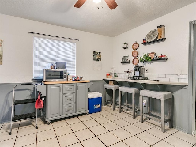 kitchen with ceiling fan, a kitchen breakfast bar, kitchen peninsula, a textured ceiling, and gray cabinets