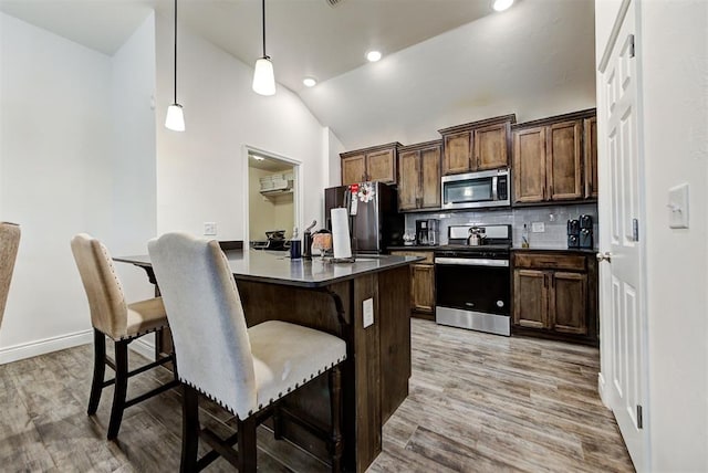 kitchen with light hardwood / wood-style flooring, decorative backsplash, appliances with stainless steel finishes, decorative light fixtures, and a breakfast bar area