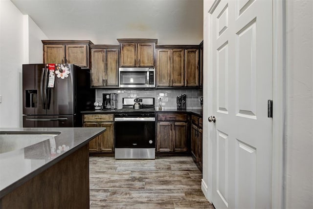 kitchen with tasteful backsplash, dark stone counters, light hardwood / wood-style floors, and appliances with stainless steel finishes