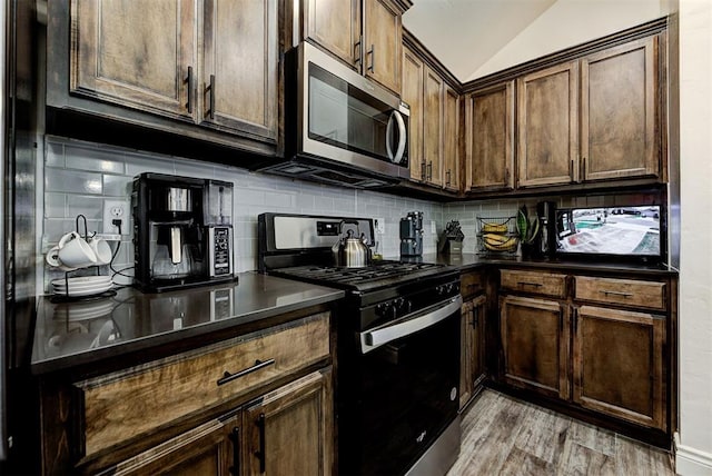 kitchen featuring light wood-type flooring, tasteful backsplash, dark brown cabinets, stainless steel appliances, and vaulted ceiling