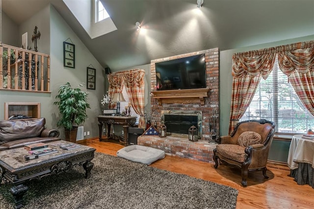 living room with a fireplace, wood-type flooring, a skylight, and high vaulted ceiling