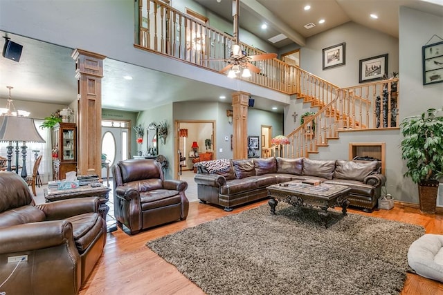 living room with ceiling fan with notable chandelier, light wood-type flooring, high vaulted ceiling, and decorative columns