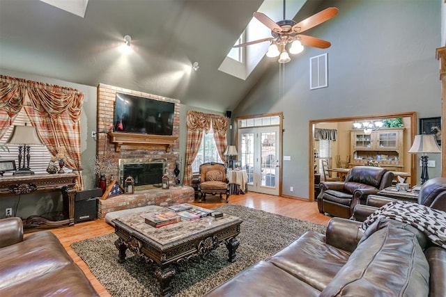 living room featuring a brick fireplace, high vaulted ceiling, light hardwood / wood-style flooring, and ceiling fan