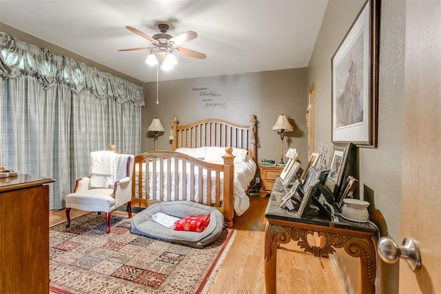 bedroom with ceiling fan, a nursery area, and wood-type flooring