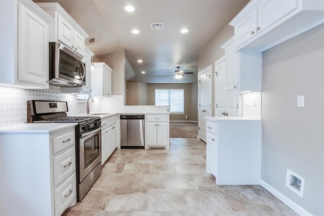 kitchen with sink, kitchen peninsula, ceiling fan, appliances with stainless steel finishes, and white cabinetry