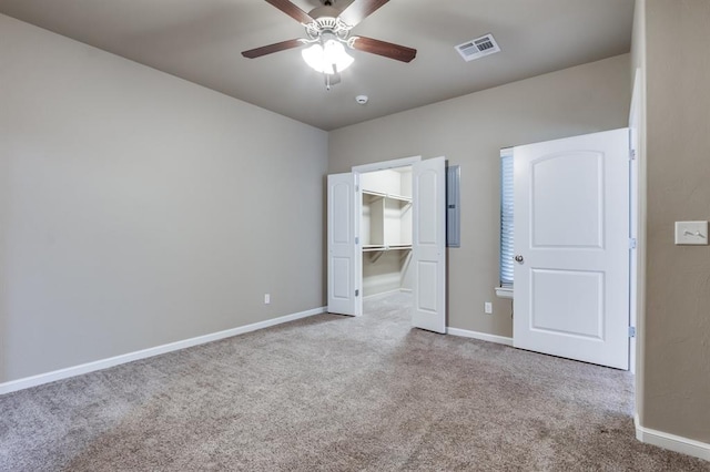 unfurnished bedroom with ceiling fan, a spacious closet, light carpet, and a closet