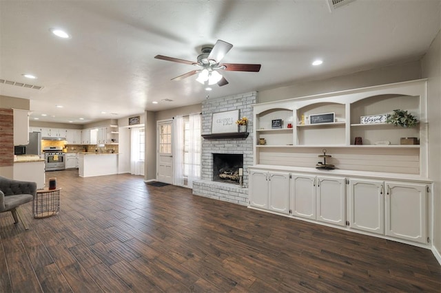 living room with a brick fireplace, ceiling fan, and dark wood-type flooring